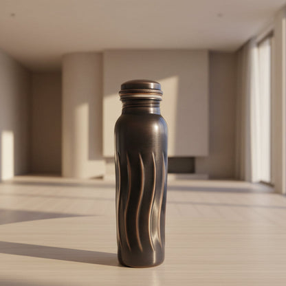 Black glass bottle with decorative design on a tiled floor