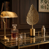 Decorative table with a lamp, cocktail shaker, and leaf-shaped object in a room with bookshelves.