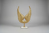 Gold winged sculpture on a white marble base against a beige wall.